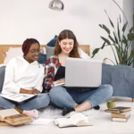 two-young-teenage-girls-sitting-floor-near-bed-studying-using-laptop_1157-51960