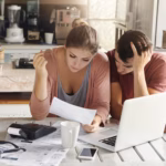 young-couple-doing-paperwork-kitchen-frustrated-woman-reading-document-together-with-her-husband-who-is-holding-his-head-desperation-sitting-table-with-laptop_273609-1654
